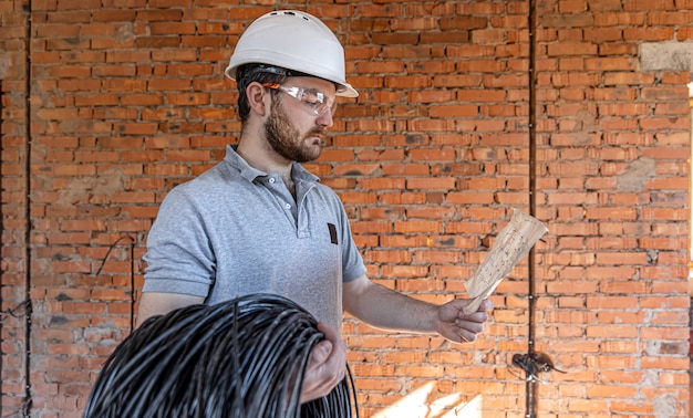 ANTONIO RULL CAPLLOCH -  - electrician examines construction drawing while holding electrical cable his hand work site